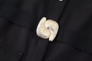 Detailed macro shot of golden textured metal button on elegant black midi dress