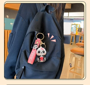 Detail of cute panda keychain with pink strap attached to a black canvas backpack zipper