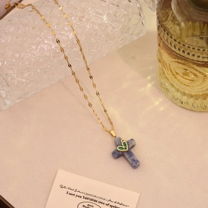 Close-up of golden cross pendant with blue stone texture and green rhinestone heart