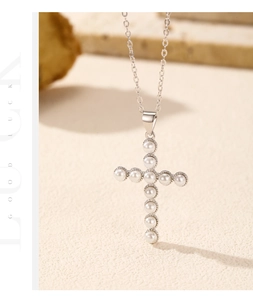 Détail du collier pendentif croix en perles avec bordure argentée perlée sur fond roche