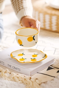 Close-up of a hand lifting a ceramic lemon pattern tea cup from a wavy-edged saucer