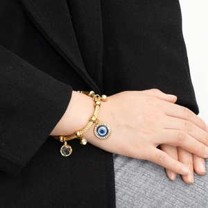 Gold twisted cable bracelet featuring evil eye charm and crystal pendants on wrist