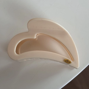 Close-up of beige hair claw clip featuring a small golden oval label with Love engraving