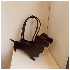 Detail of dark brown dachshund shaped shoulder bag in glossy faux leather against a wall