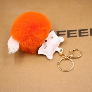 Close-up of bright orange faux fur pompom fox keychain with gold metal clasp detail