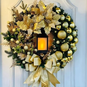 Close-up of golden Christmas wreath with glowing lantern on white door backdrop