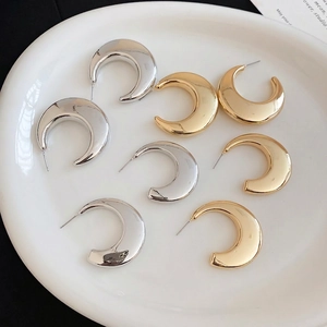 Polished gold and silver C-shaped hoop earrings set on white ceramic tray
