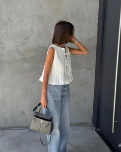 Detail of white pleated sleeveless top with tie-front detail and light wash denim jeans