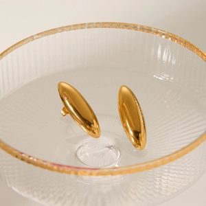 Macro shot of oval gold stud earrings with a polished mirror finish in a glass bowl