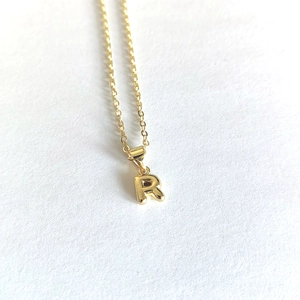 Close-up of minimalist gold initial R pendant necklace on white textured background