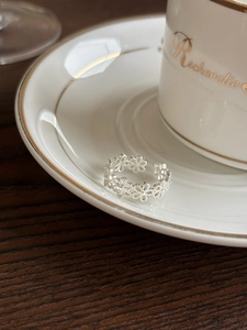 Detailed view of silver flower open ring on a wooden table near a white coffee cup