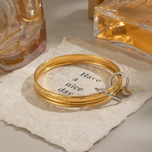 Three-piece stackable 18K gold stainless steel heart bracelets on a textured background