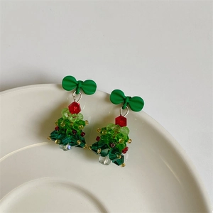 Detail of beaded Christmas tree earrings with a green bow on a white ceramic tray