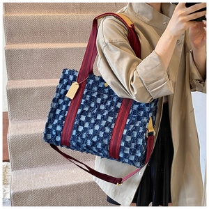 Detail of denim tote bag with red fringe and gold hardware on minimalist staircase