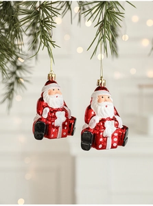 Detail of Santa Claus ornaments hanging on green pine branches with warm bokeh lights