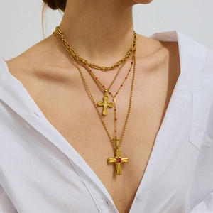 Détail de colliers superposés en or avec croix et pierre rouge sur une chemise blanche