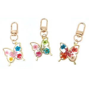 Three gold butterfly keychains with colorful real dried flowers in resin, white background