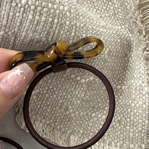 Close-up of tortoise shell bow hair tie with dark brown elastic on beige linen background