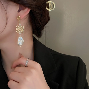 Macro detail of gold hollow-out knot earrings with elegant baroque pearls on a female model