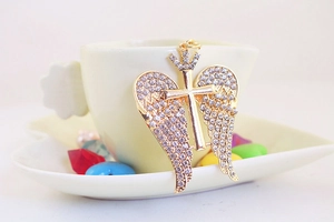 Macro shot of gold angel wings and cross pendant with rhinestones on a coffee cup edge