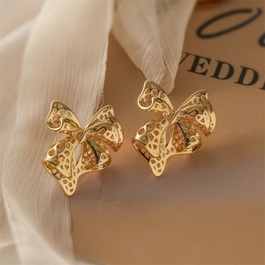 Close-up of golden hollow bow earrings on soft beige fabric background with elegant details