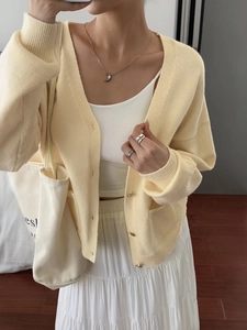 Detail view of light yellow knit cardigan paired with a white skirt and canvas bag
