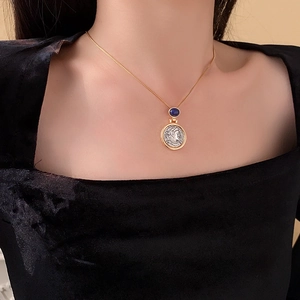 Detail of vintage coin pendant with deep blue gemstone on a gold chain necklace
