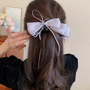 Rear view of a model wearing the purple satin bow hair clip with a central pearl accent