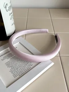 Close-up of pink satin padded headband texture with black woven label on beige surface