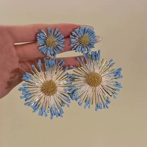 Detail view of blue and gold floral earrings with textured petals on a beige background