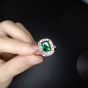 Elegant rose gold emerald cut green gemstone ring with pavé diamond halo worn on finger