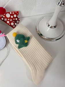 Detailed macro view of cream ribbed socks featuring a plush green Christmas tree patch