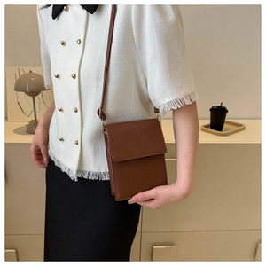 Petit sac rectangulaire marron avec rabat et bandoulière porté sur une veste blanche