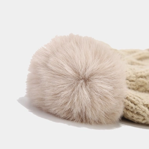 Close-up of the soft faux fur pom-pom on top of a beige cable-knit winter beanie