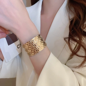 Detail of a wide gold metal bracelet with intricate woven texture worn by a model