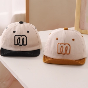 Close-up of soft-brim baby baseball caps with embroidered 'm' and textured cotton fabric