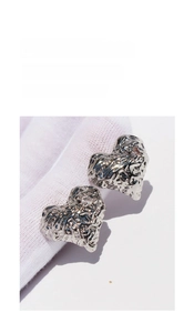 Detailed close-up of silver heart stud earrings with irregular crushed metal texture
