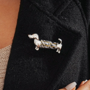 Close-up of a silver dachshund brooch with tricolor rope on a black wool coat collar