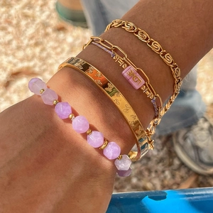 Golden stackable bracelets with amethyst beads and butterfly engraving worn in sunlight