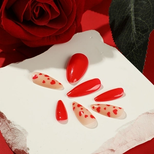 Red and white press-on nails with heart designs displayed on a marble stone base