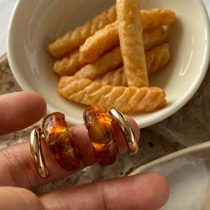 Macro shot of amber resin C-shape earrings with gold metal base held by fingers