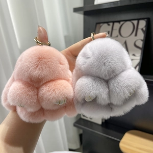 Detail of soft pink and grey plush rabbit keychains with gold metal clasp held in hand