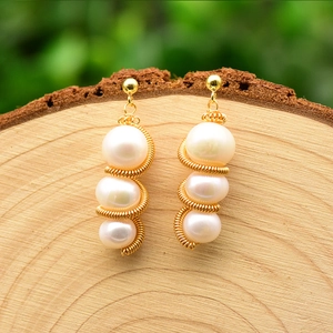 Detail of natural pearl earrings with gold spiral wire design on a rustic wooden base