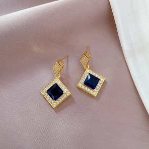 Detailed macro view of gold-plated earrings with blue square stones and crystal accents