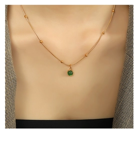 Detail of green aventurine pendant on gold snake chain worn over a textured suit