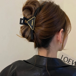 Detail of a matte black triangle hair claw clip with golden POWER letter on dark hair