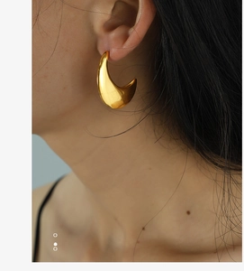 Macro close-up showing thick crescent moon golden stud earrings with polished finish