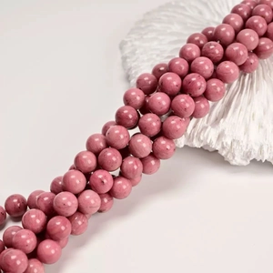 Macro shot of natural pink rose stone round beads with unique stone textures on white surface