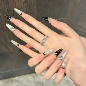 Close-up of pink press-on nails with black bows, silver glitter, and rhinestone details