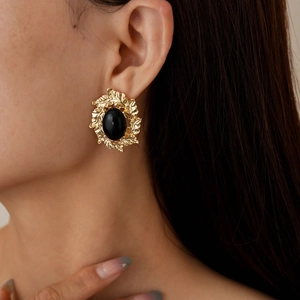 Retro gold leaf studs with black oval gemstone inlay worn by a model in warm lighting